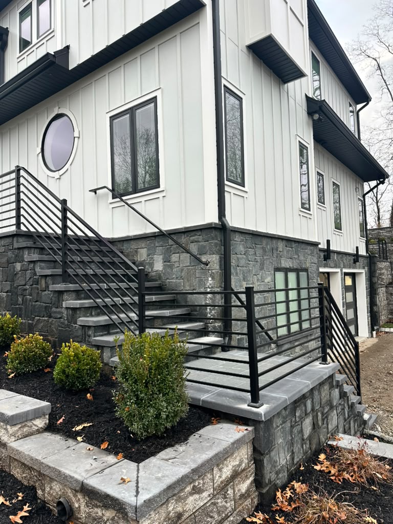 Black horizontal-bar railing on the stone stair run of a white board-and-batten modern farmhouse
