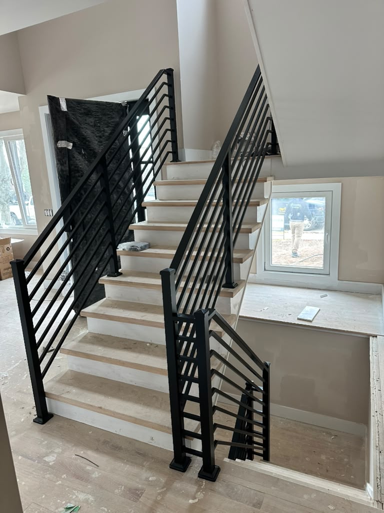 Interior stair railing with black flat horizontal bars beside wood treads during construction