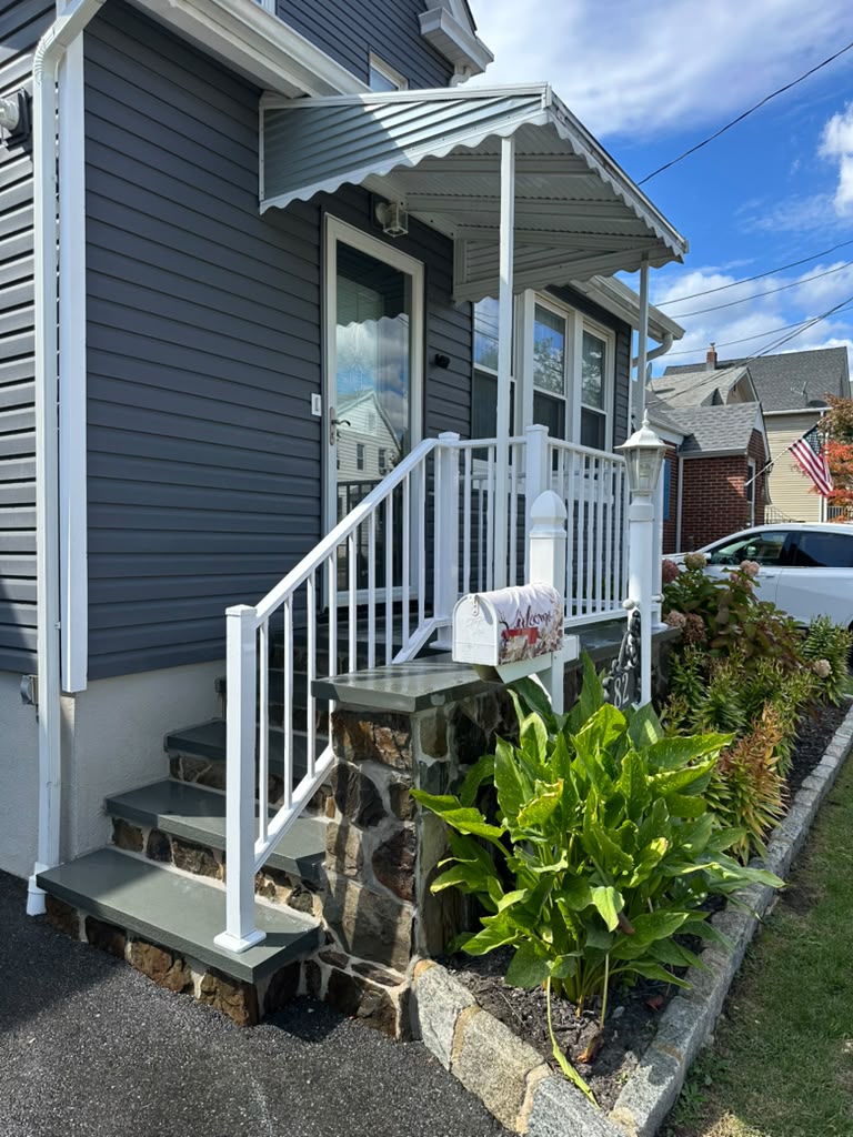 White picket railing with finial posts on the stone-veneer stoop of a gray-blue colonial home