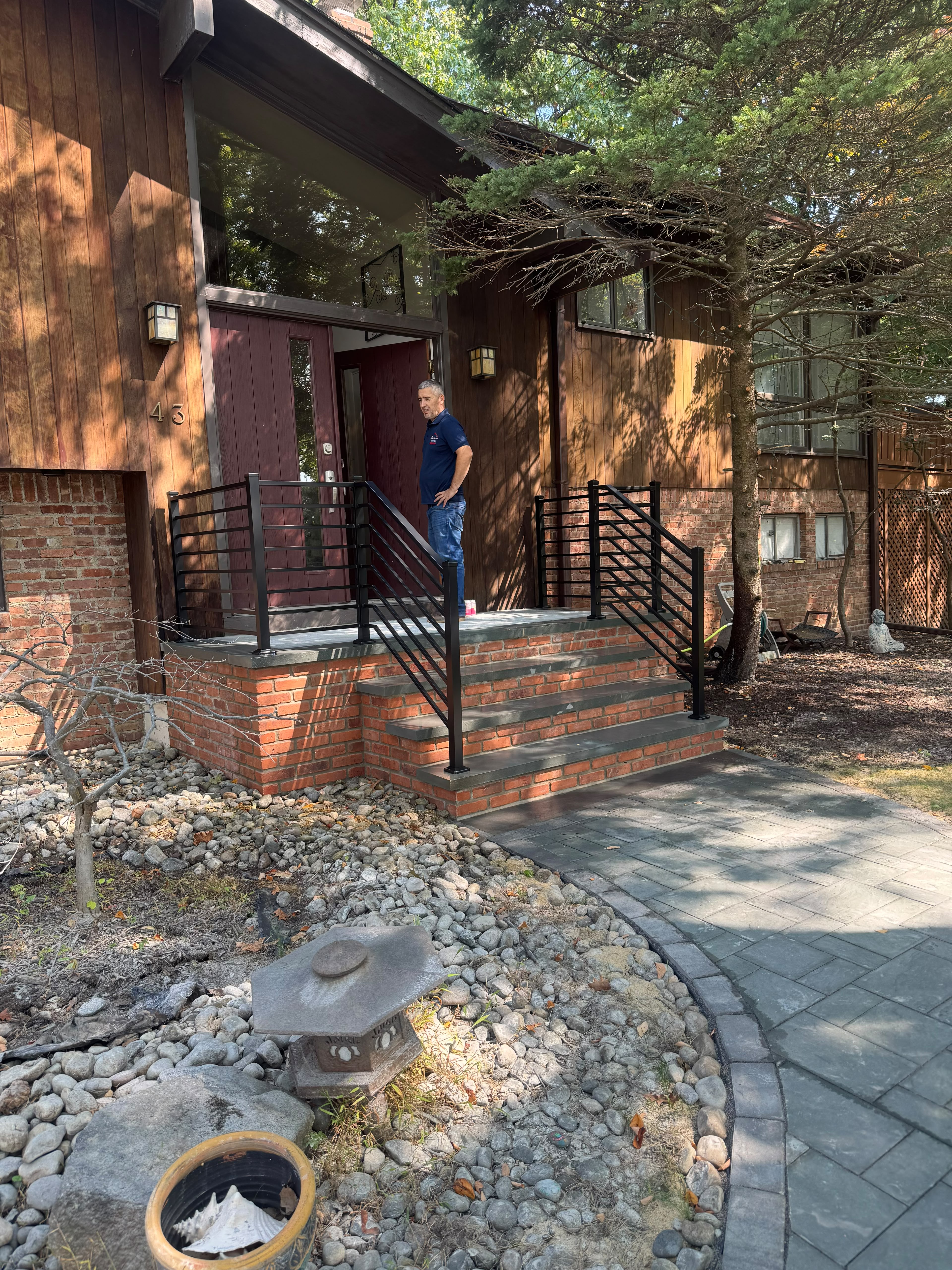 Black horizontal railing on the brick entry steps of a contemporary stained-wood and white home