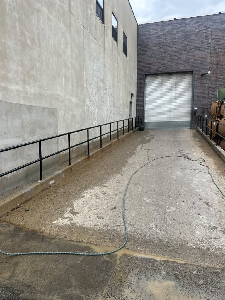 Black pipe handrail along the concrete walkway at an industrial loading area