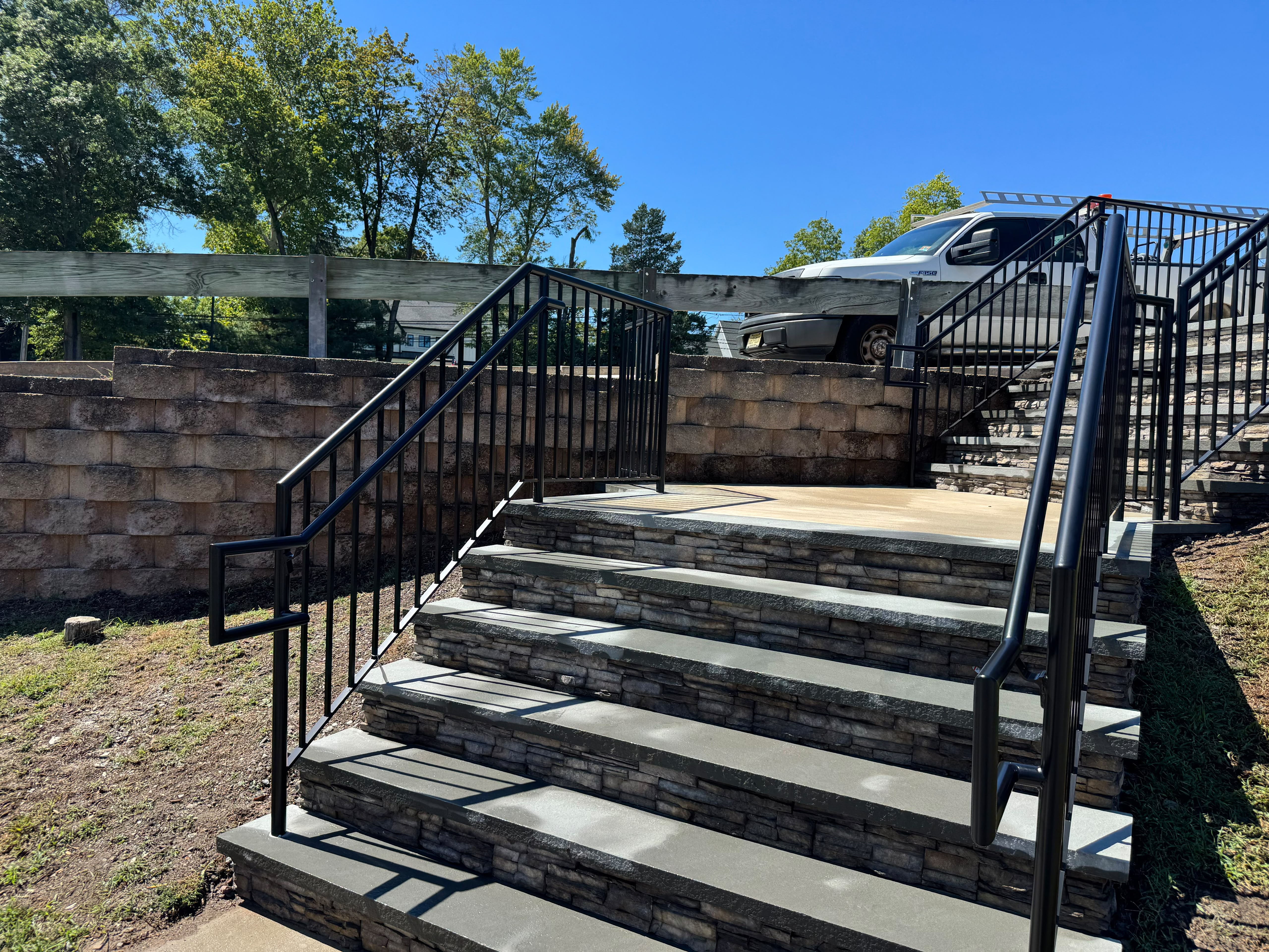 Black vertical-bar guardrail on stone-faced steps at an industrial yard