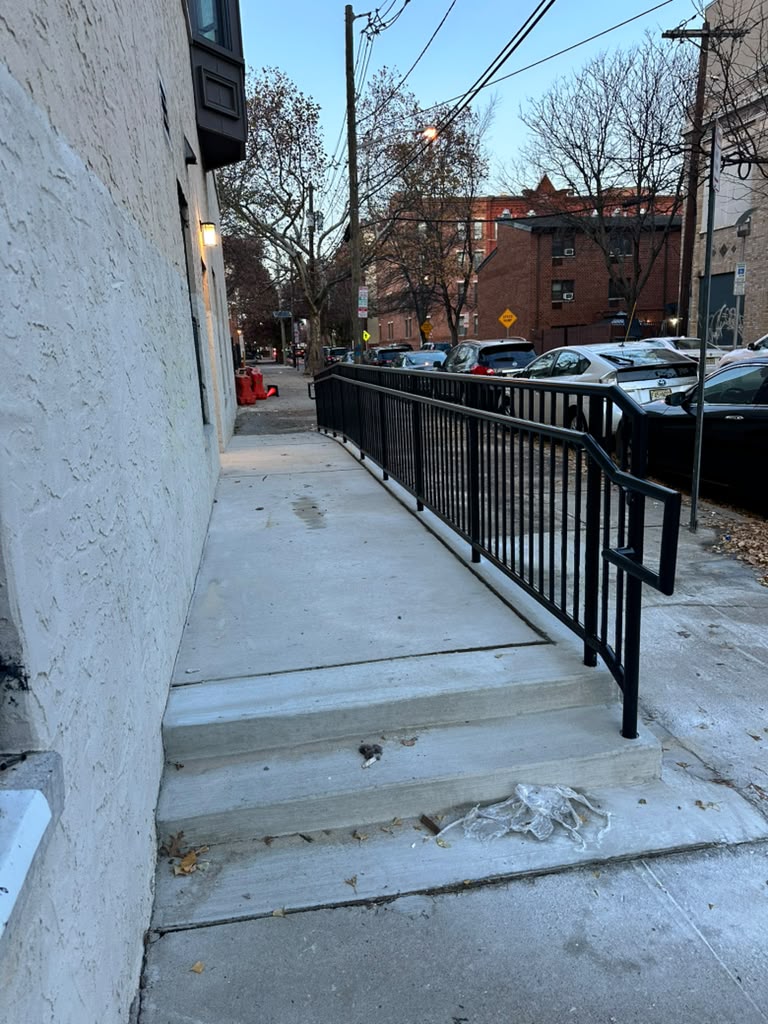 Black vertical-bar guardrail along a raised sidewalk beside a stucco commercial building