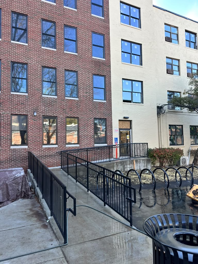 Black guardrail around the concrete ramp and bike parking area of a brick apartment building