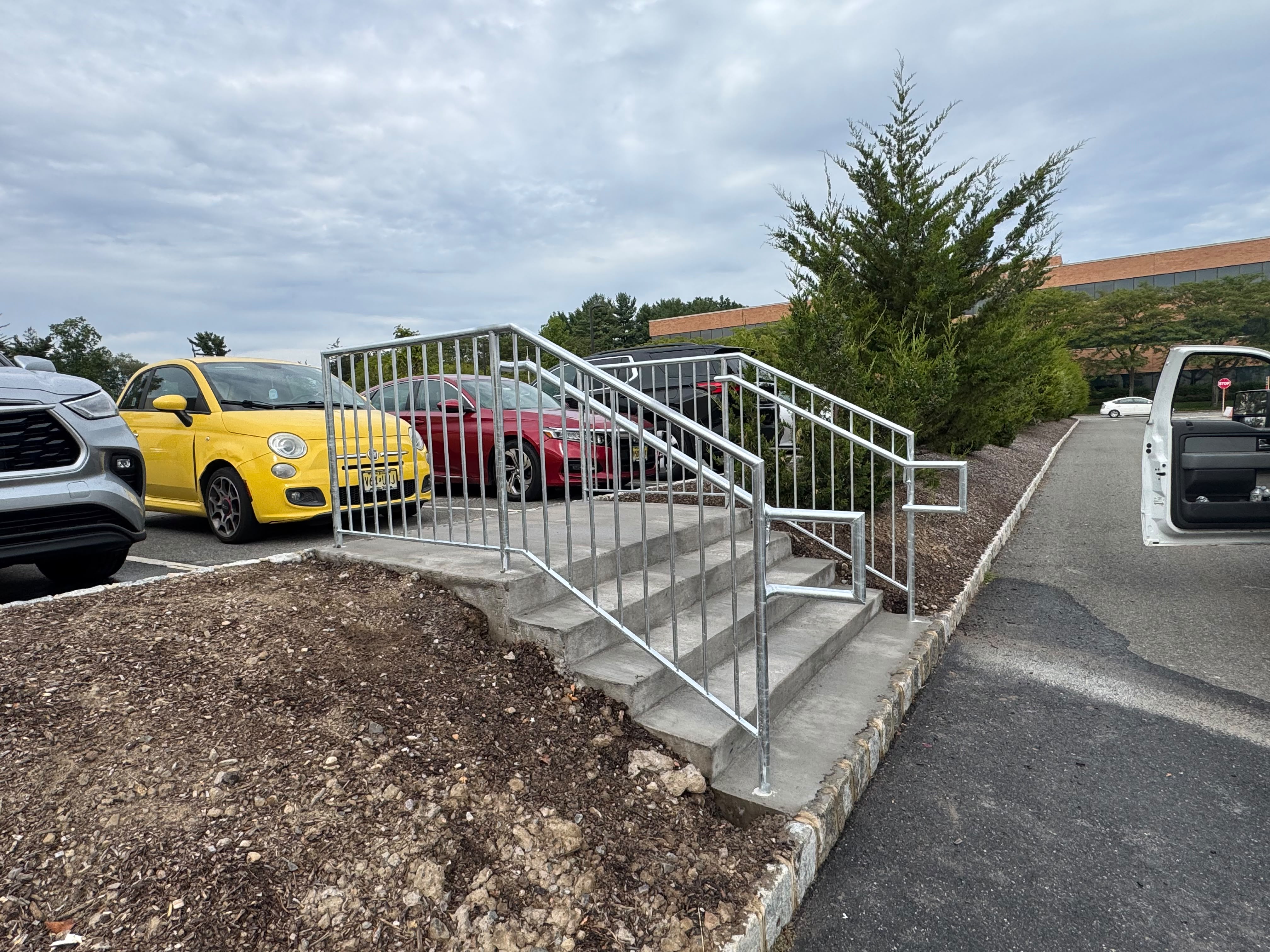 Galvanized steel handrails on the concrete steps between a parking lot and walkway