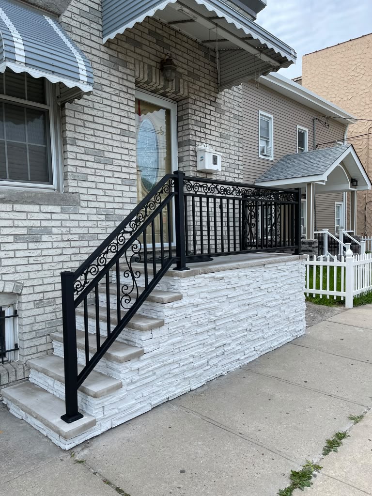 Ornate black scroll railing around the porch and steps of a brick home with white stacked-stone base