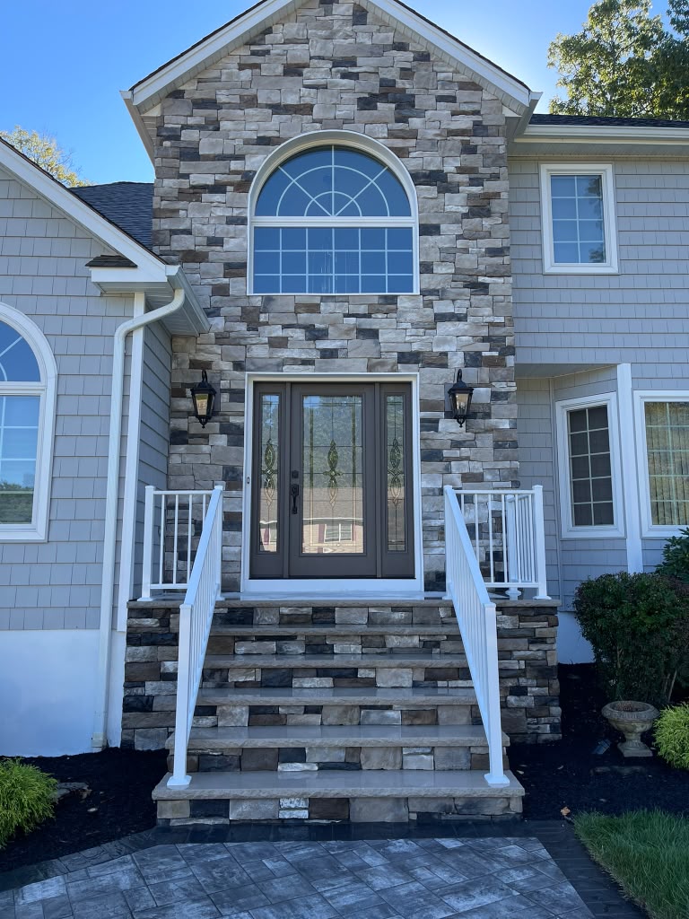 White aluminum picket railings on both sides of a ledgestone entry with a bronze glass door