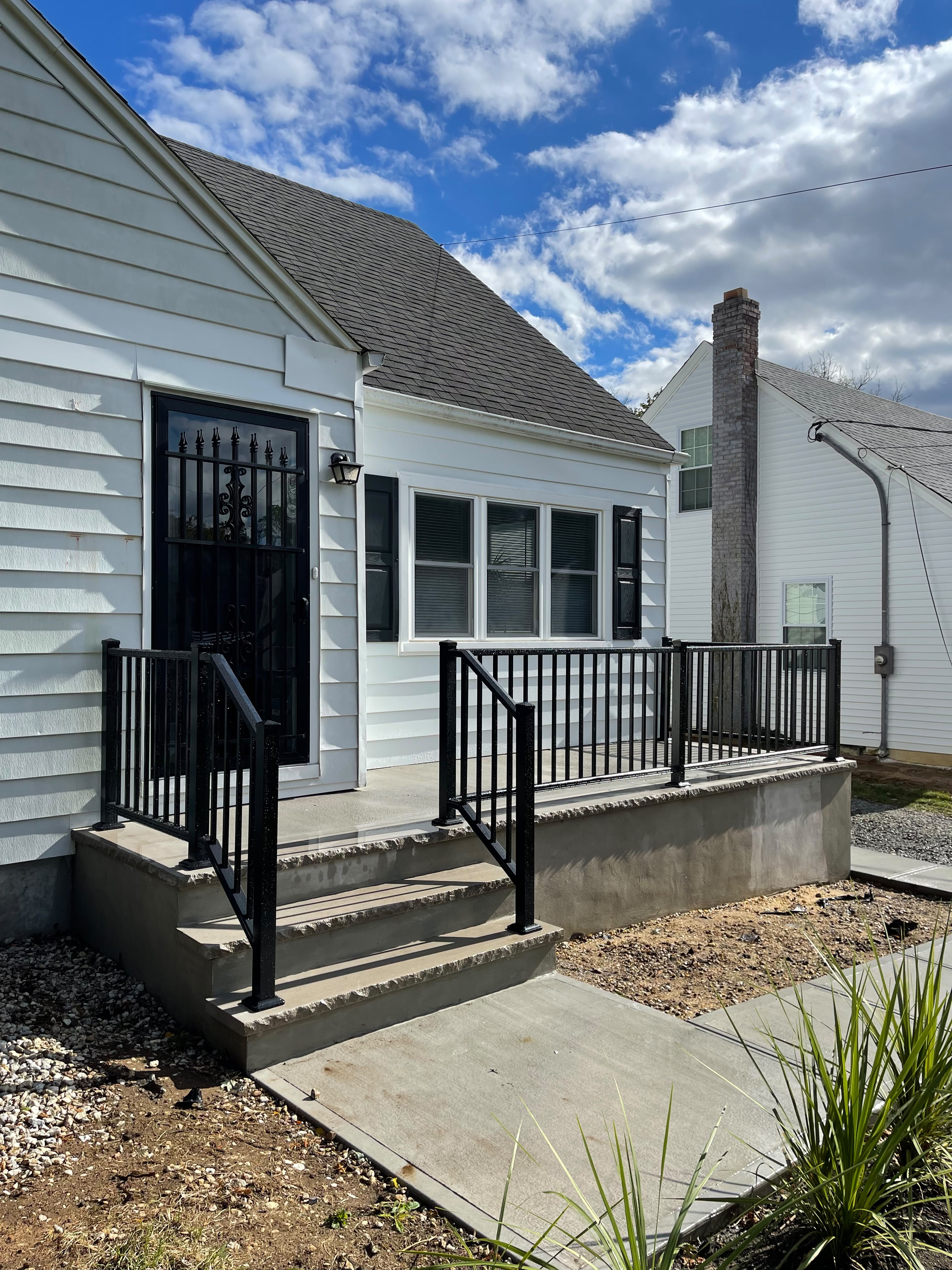 Black railing around a raised rear concrete porch with steps at a white clapboard home