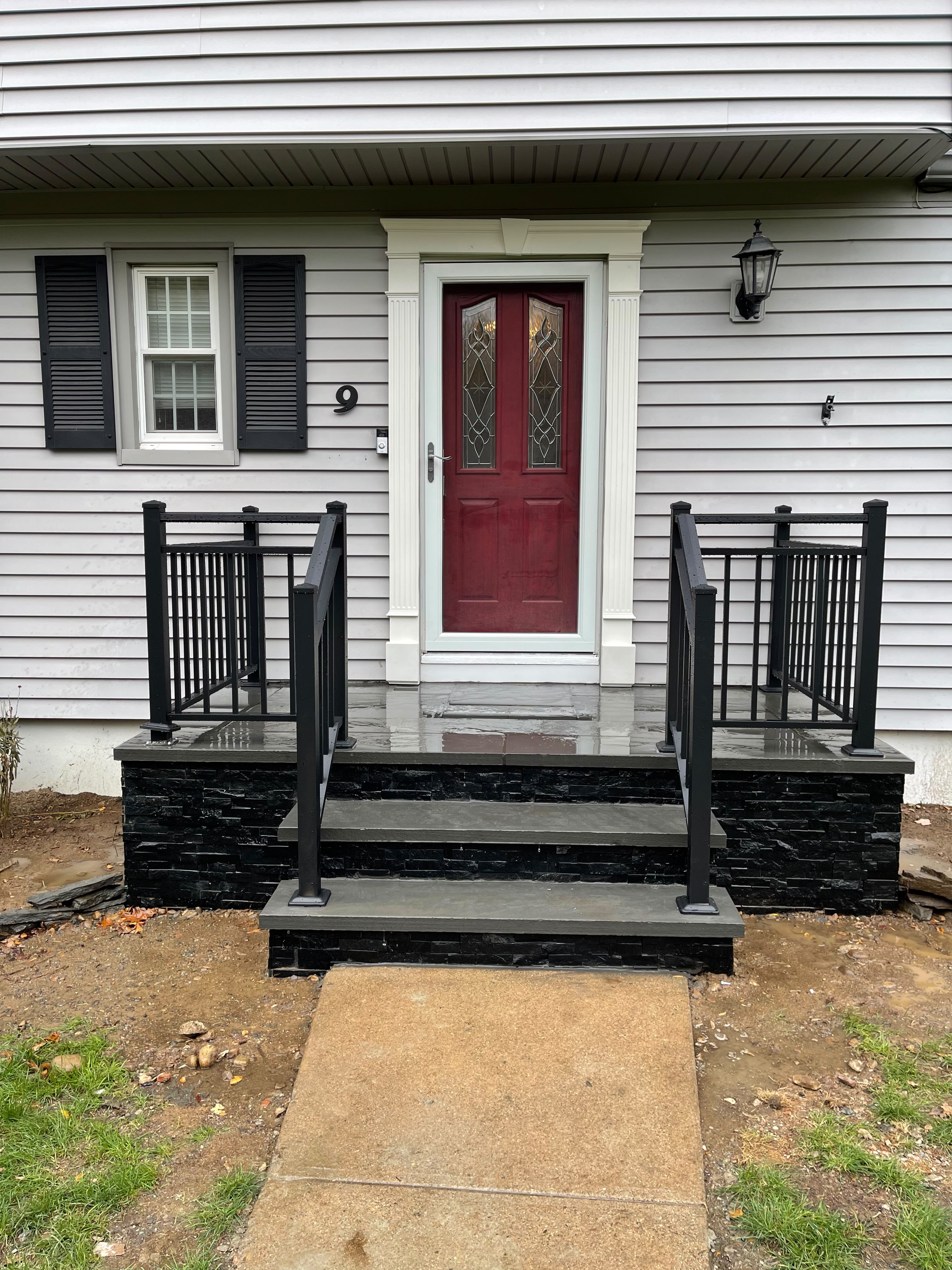 Decorative black basket-picket railings on both sides of new black stacked-stone entry steps