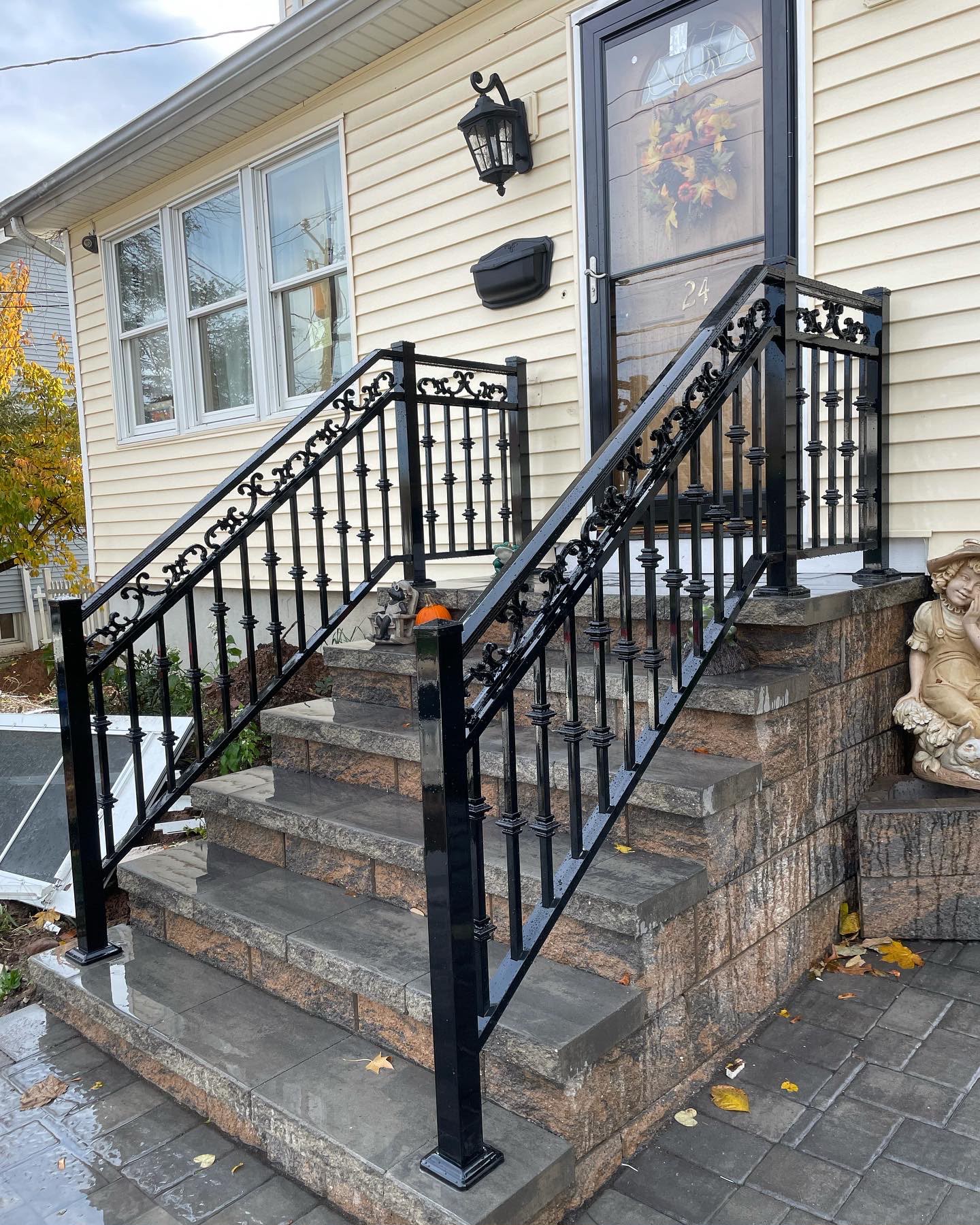 Ornamental black scroll railing down the stone entry steps of a cream clapboard home