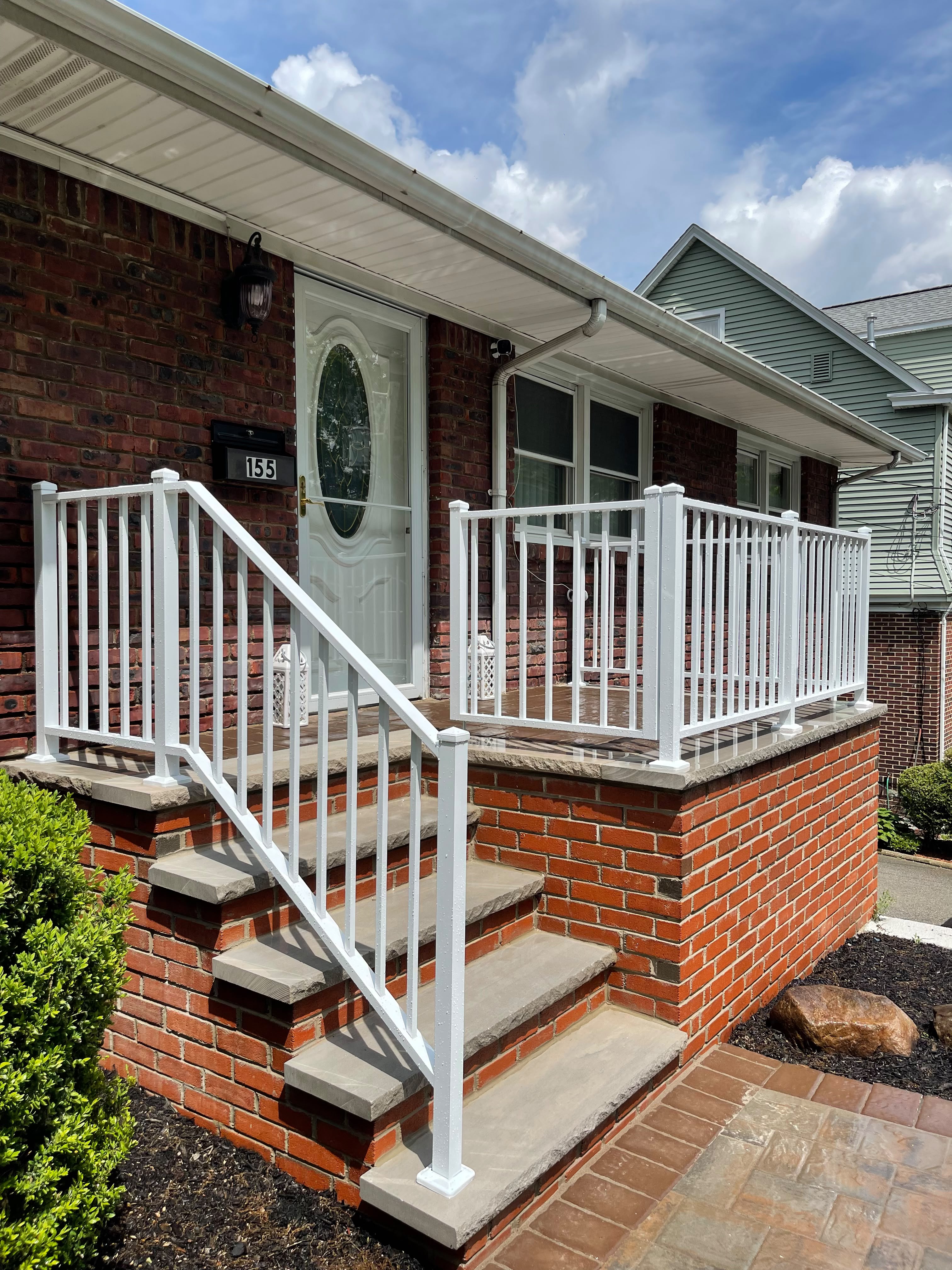White aluminum railing on the brick porch and entry steps of a red brick home