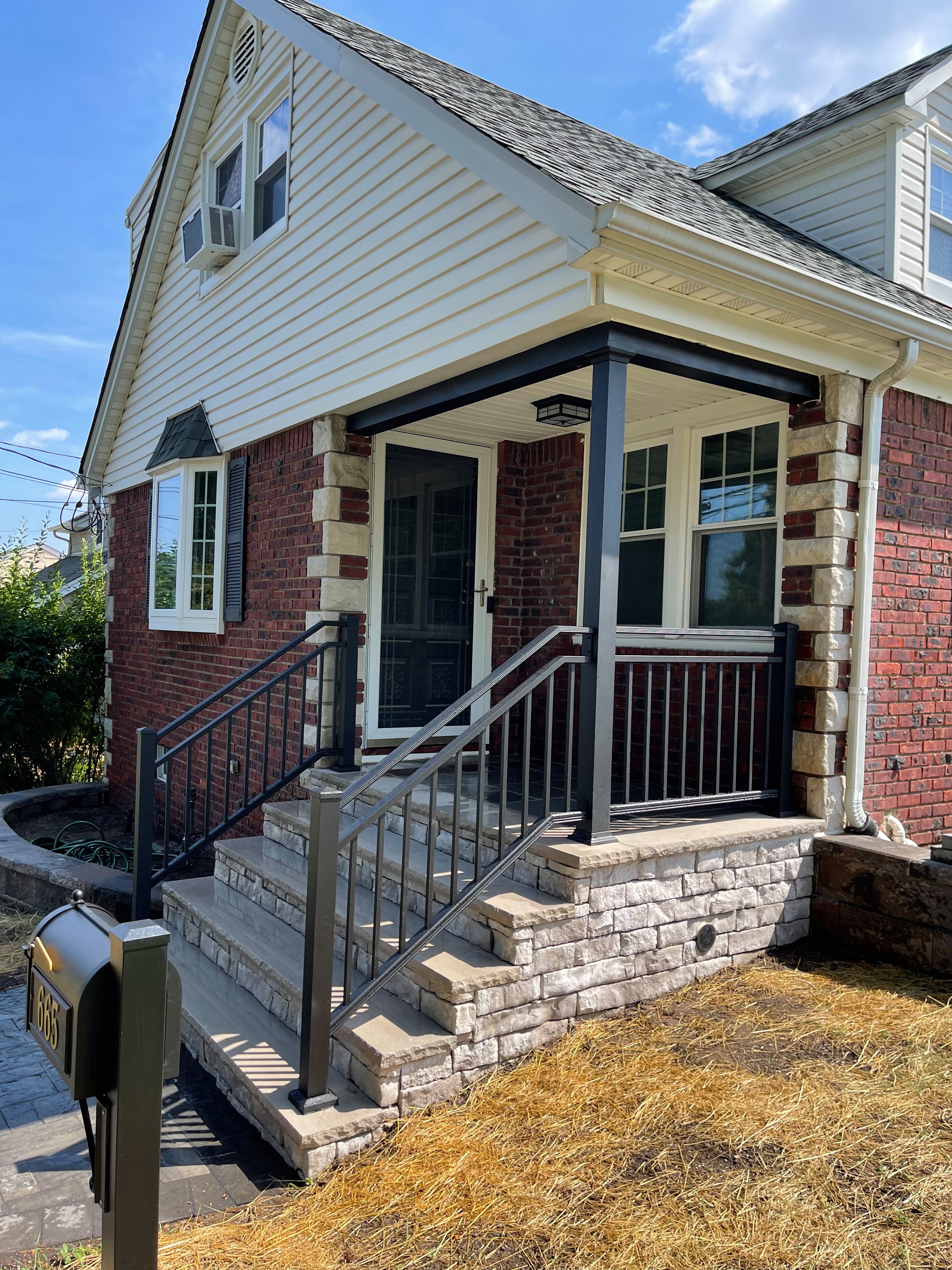 Black handrail and porch railing on the stone-veneer steps of a cape-style home