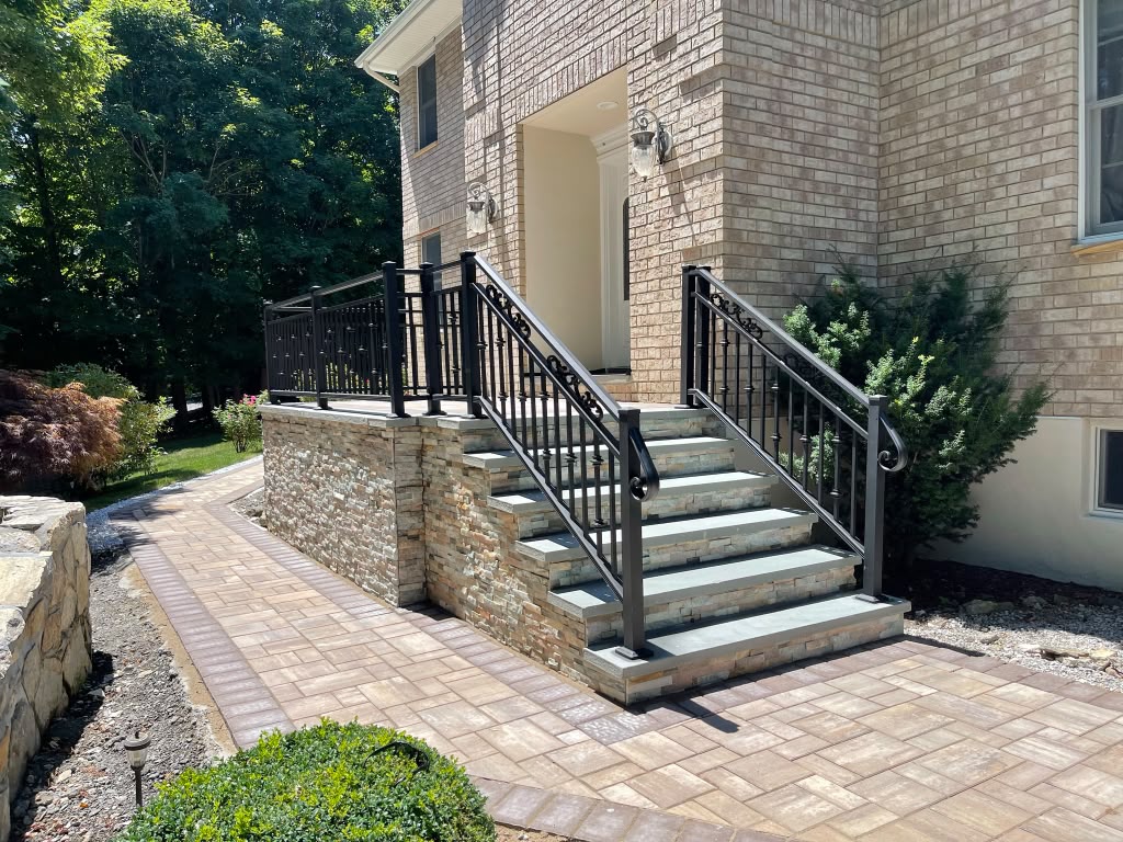 Ornamental black scroll railing around a stone-veneer entry terrace with paver walks