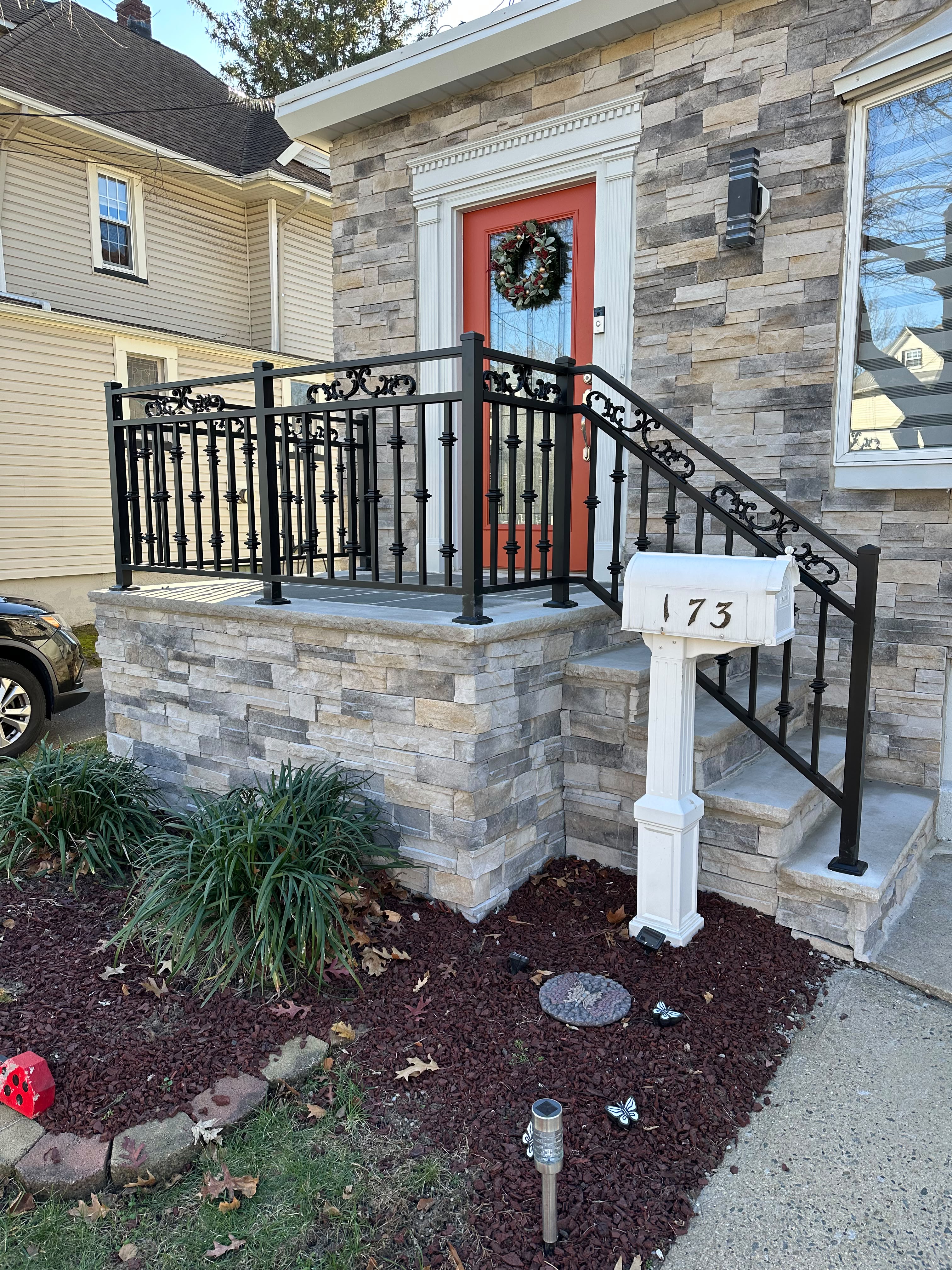 Ornamental black scroll railing on ledgestone entry steps and porch with a red door