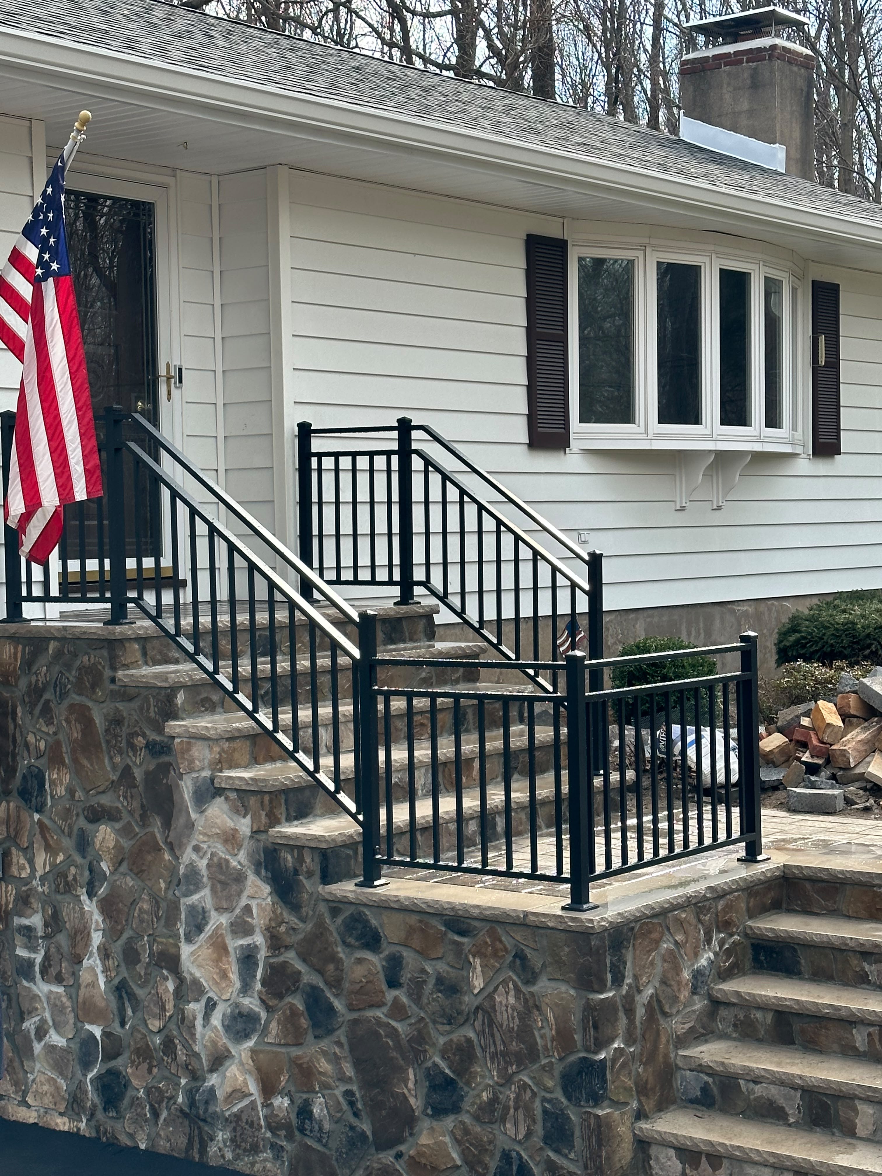 Black railing installed down the fieldstone entry steps of a white clapboard home