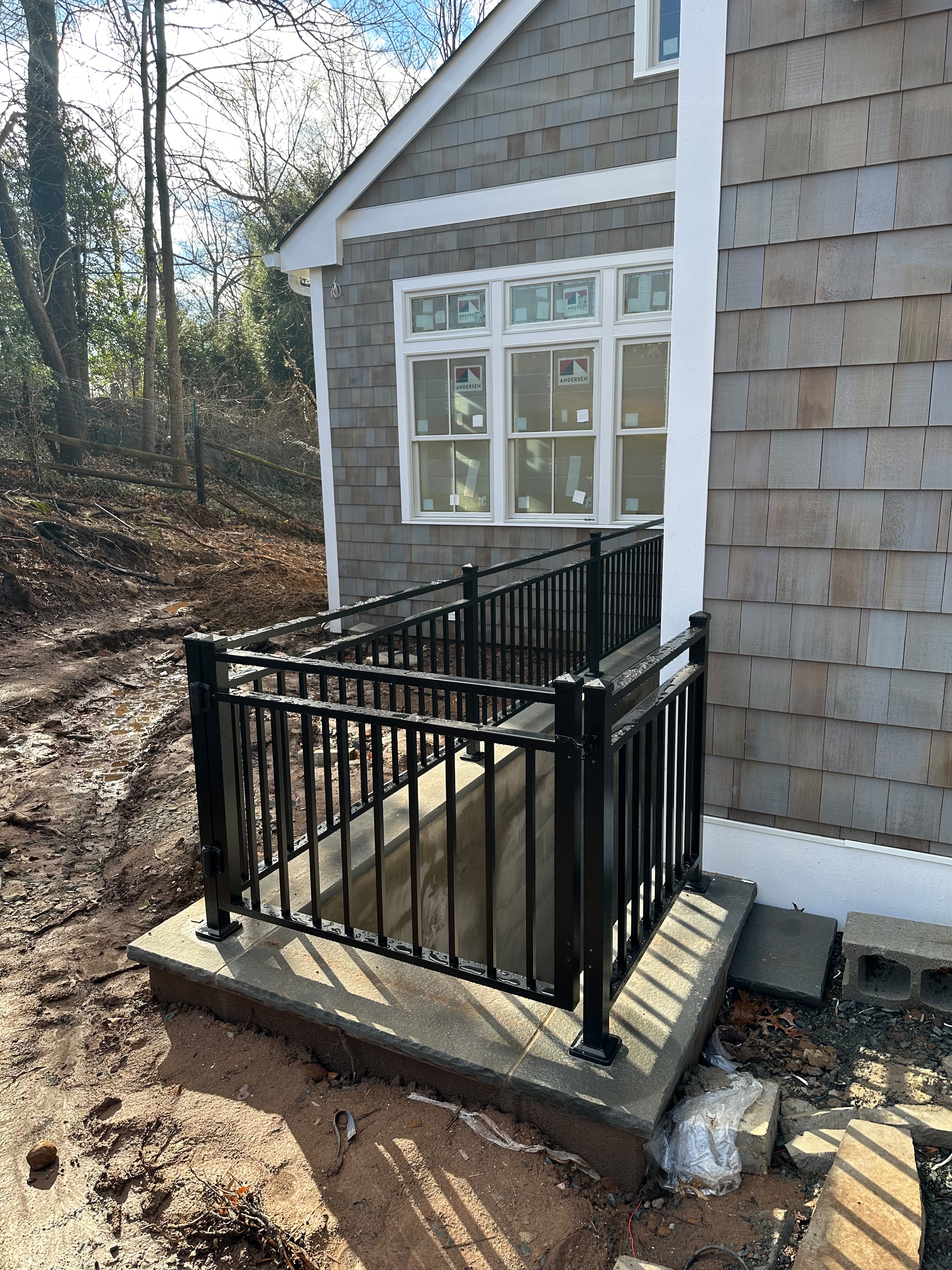 Black picket railing on the front stone steps and porch of a new cedar-shingle home