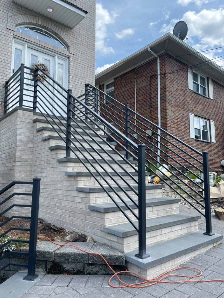 Black horizontal rod railing with round posts on gray stone entry steps and landing