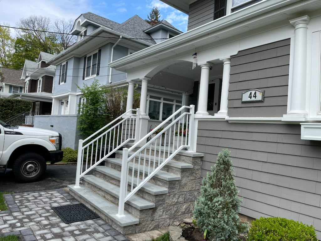 White railing on the stone steps and covered porch of a gray-blue cedar-sided home