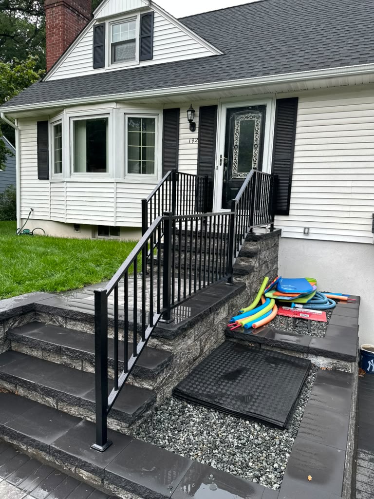 Black railing on the stone front steps of a white cape-style home with black shutters