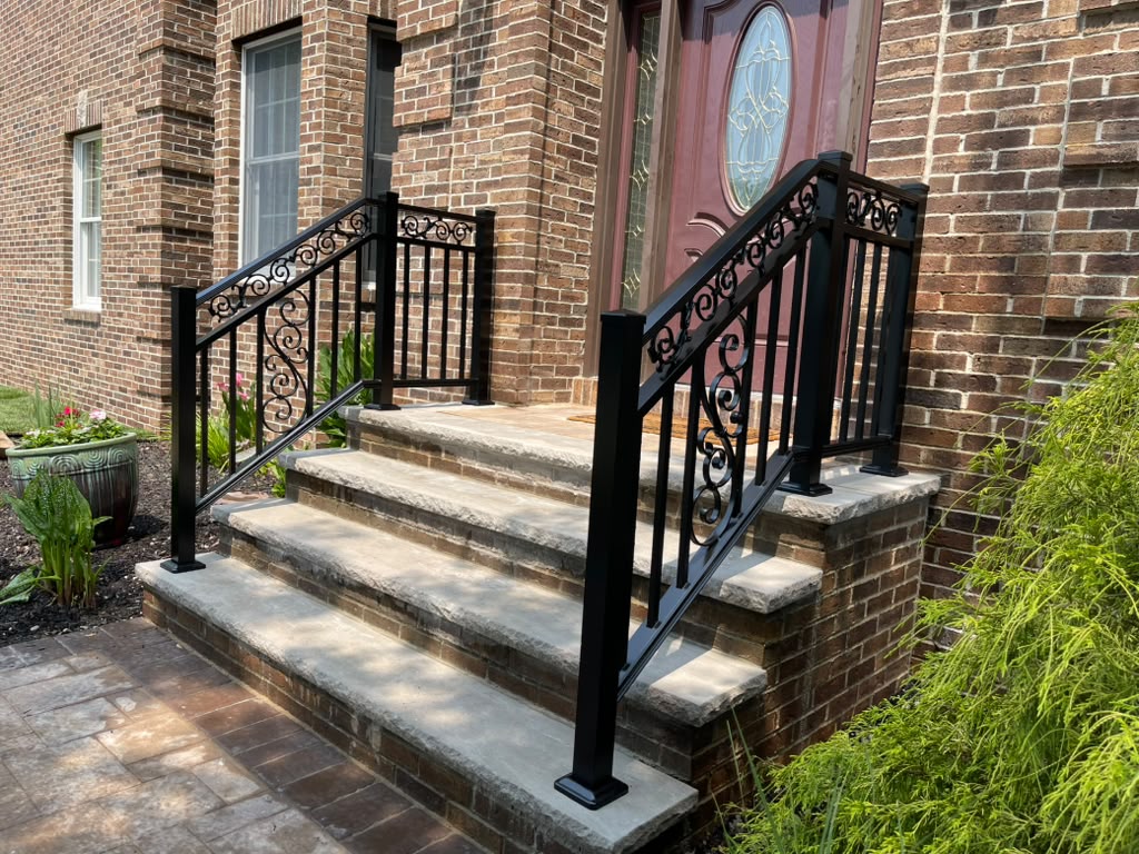 Ornamental black scroll railing on the brick entry steps of a home with arched brick detailing