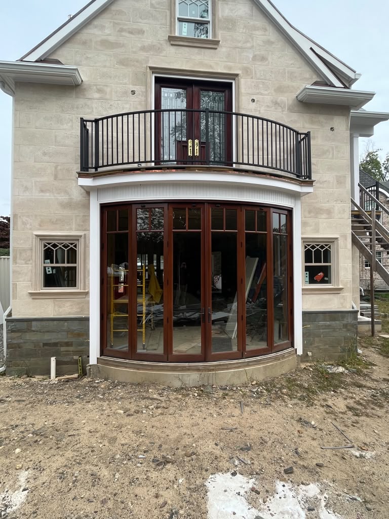 Black curved balcony railing above a bowed window wall at a new stone-faced home