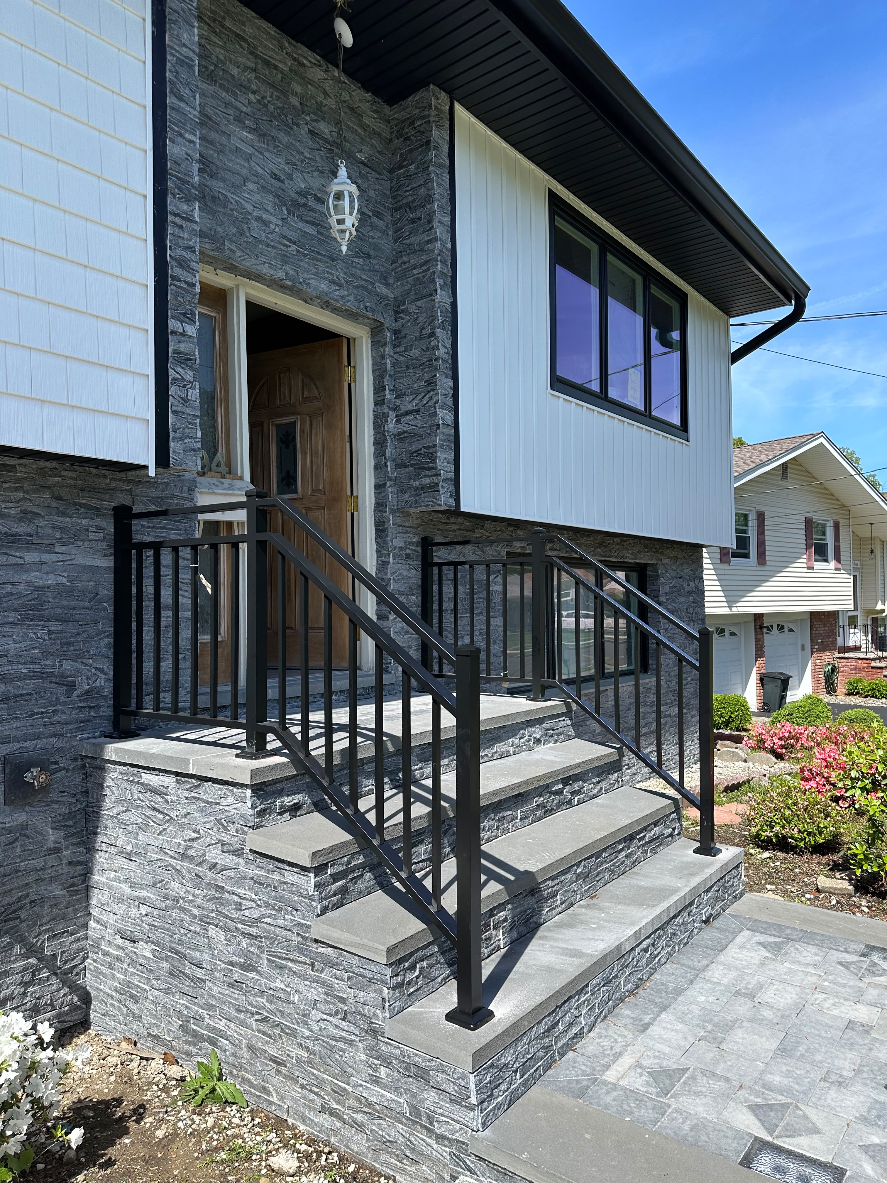 Black picket railing on the gray ledgestone entry steps of a modern white home