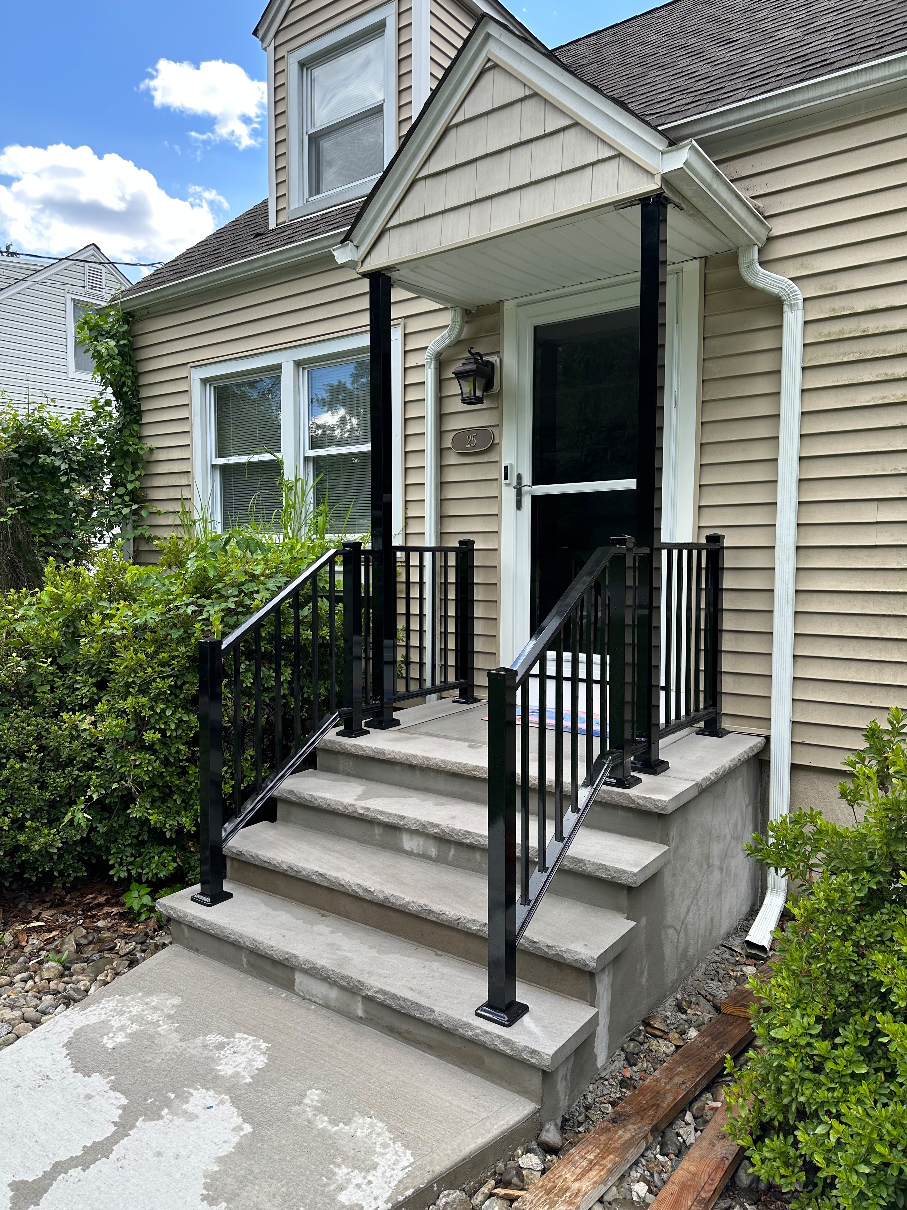 Black picket railing with capped posts on the concrete entry steps of a beige vinyl-sided home