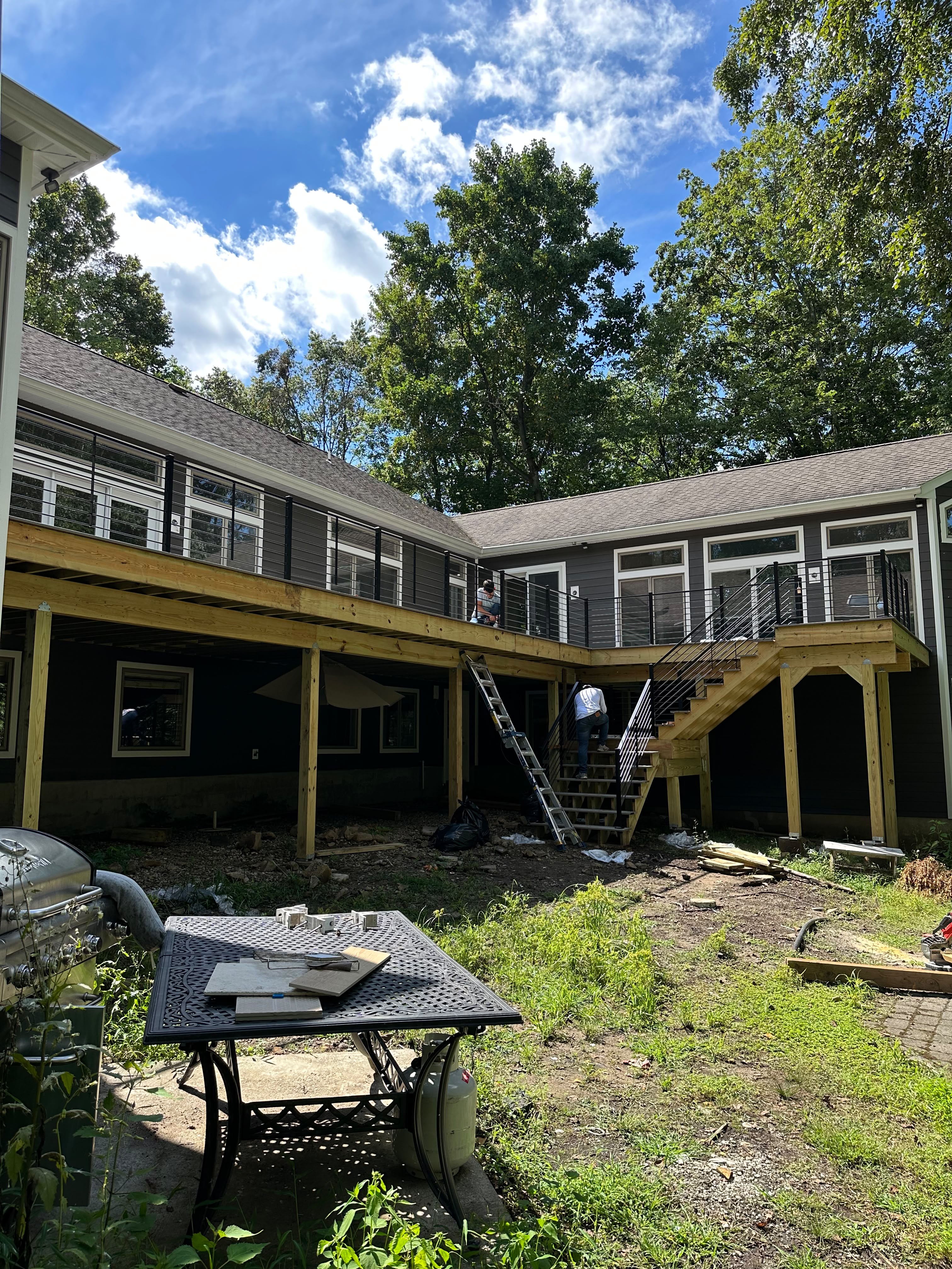 Cable railing around a large wraparound deck at a dark-sided home during construction