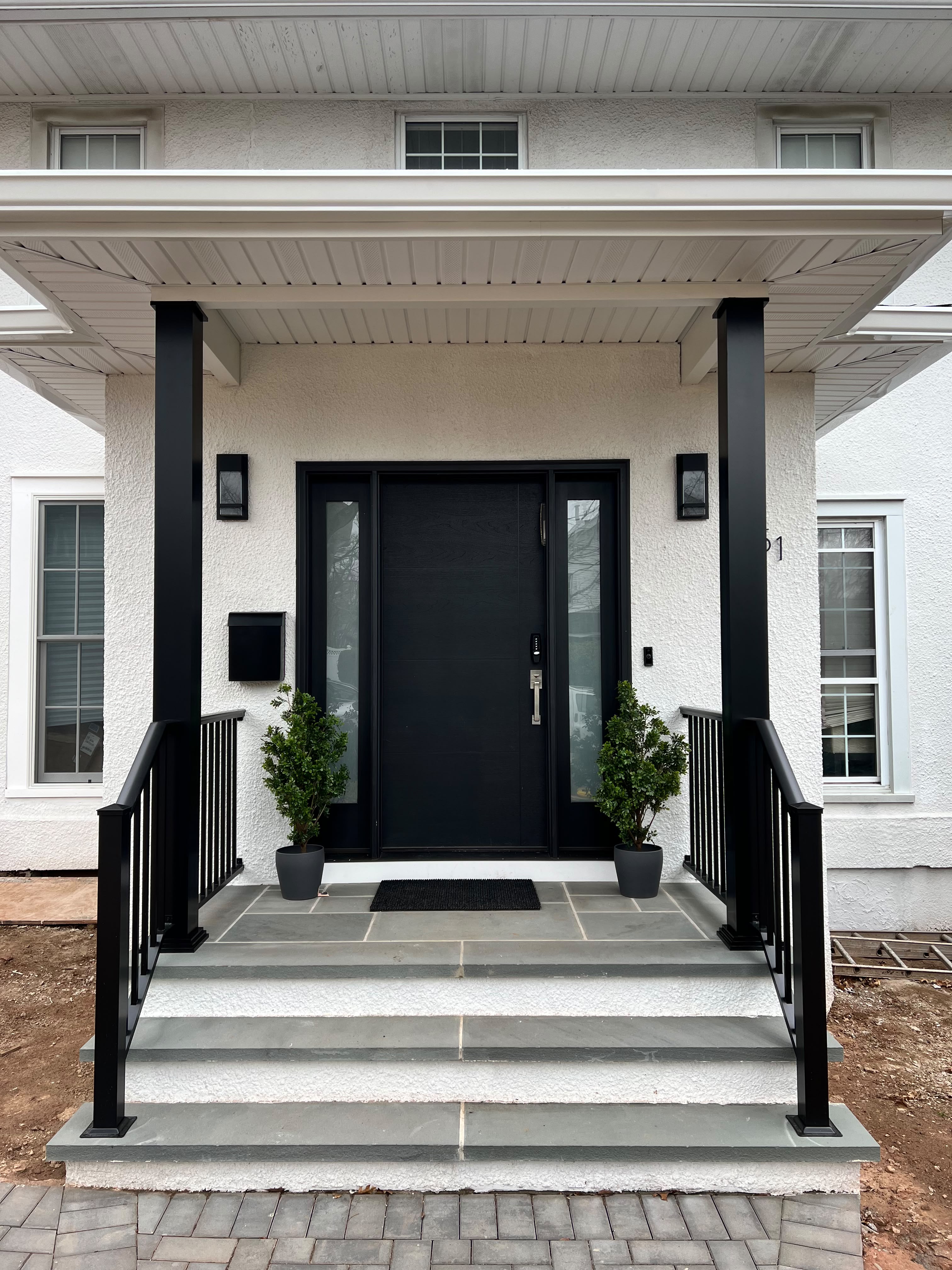 Black picket railing on the white stucco entry steps and landing of a modern home