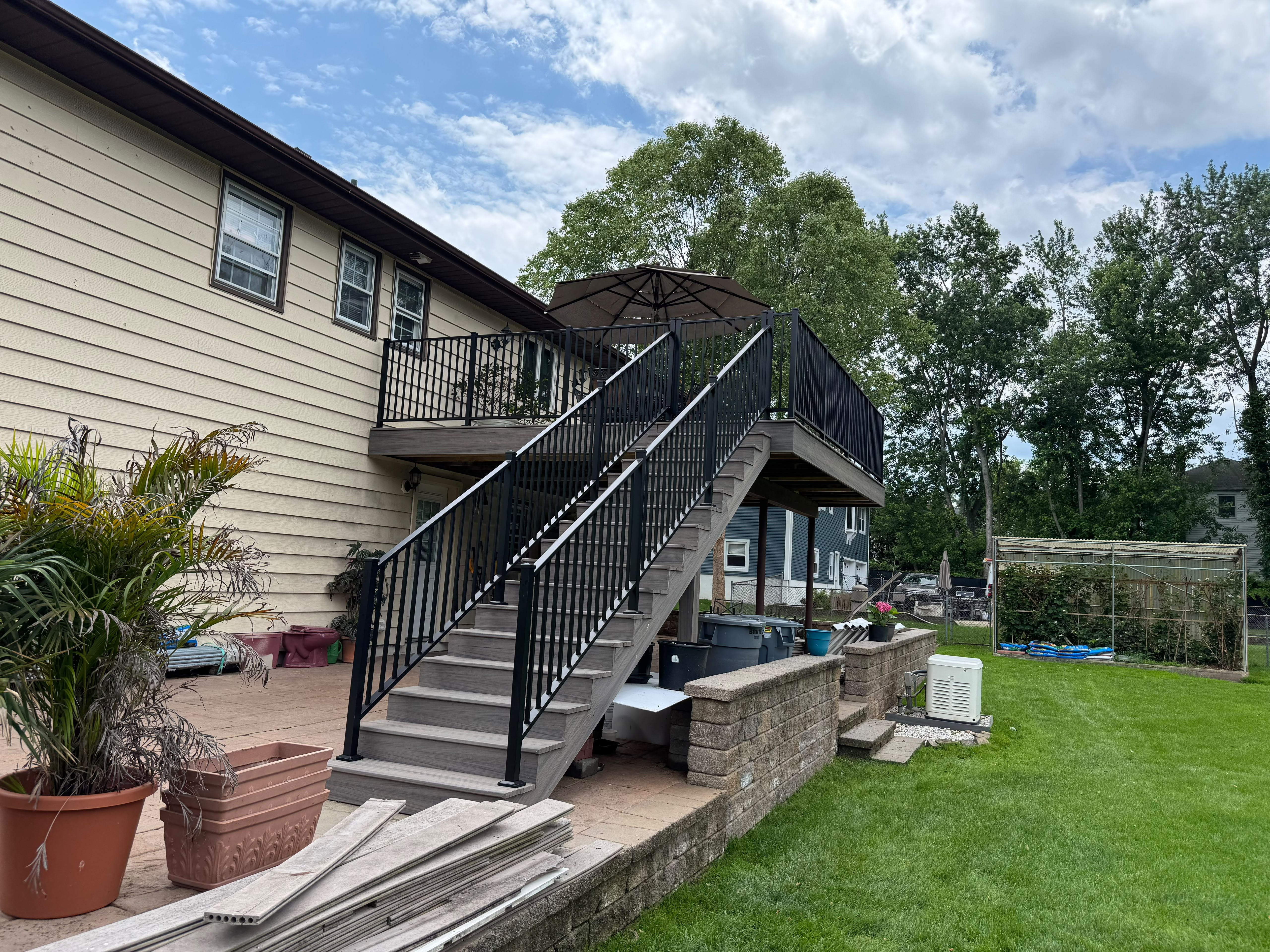 Black railing around an elevated deck and down its long stair run to a patio