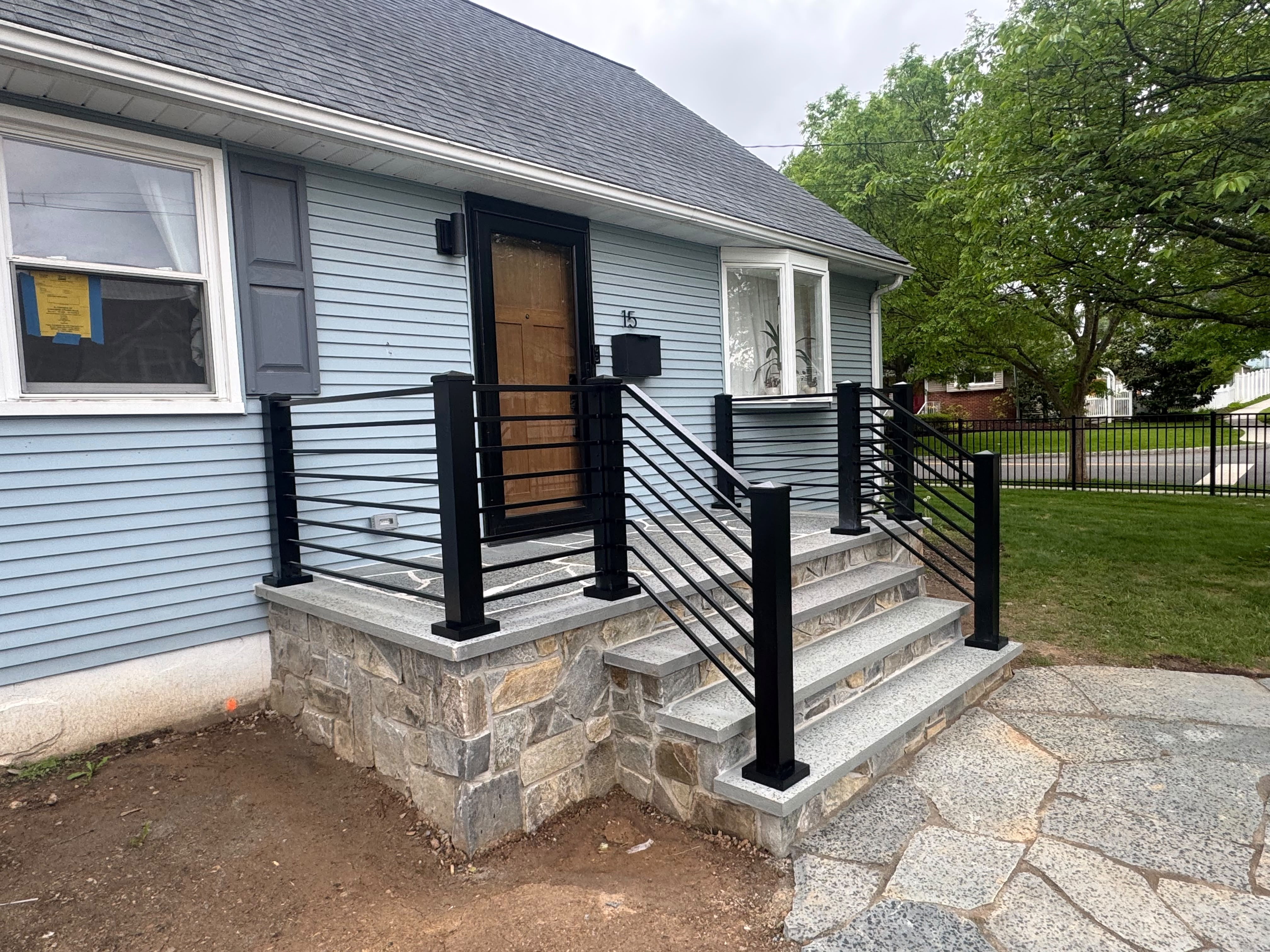 Black horizontal railing with heavy square posts on a fieldstone porch with granite treads