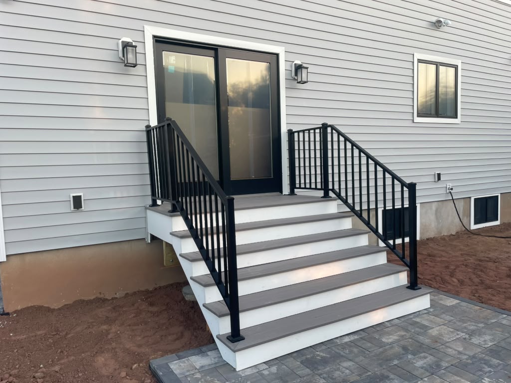 Black picket railing on both sides of new composite deck steps at a gray-green sided home