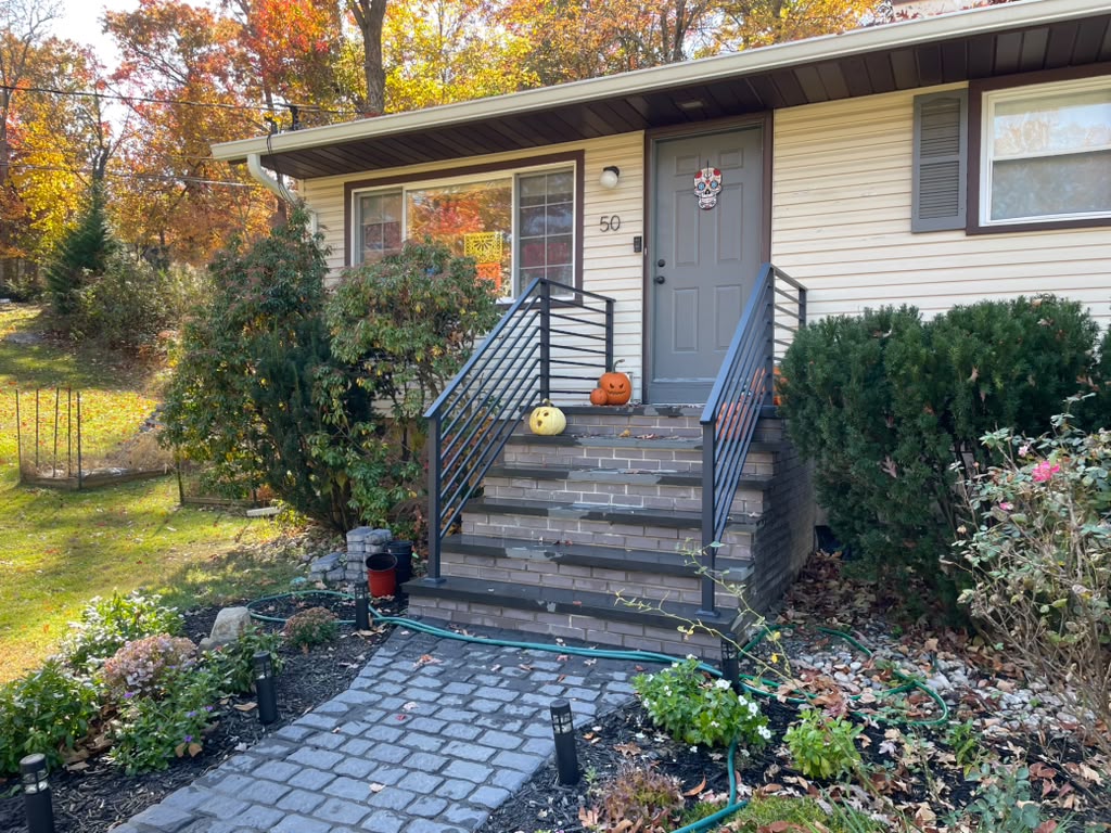 Dark bronze railing with horizontal bars and vertical accents on brick entry steps in autumn
