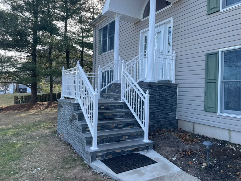 White railing with decorative balusters around a porch with a dark blue stacked-stone base